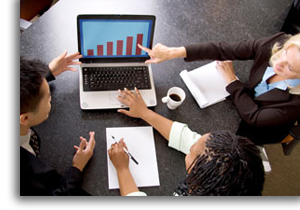 A group of people poiting at a graph on a laptop.