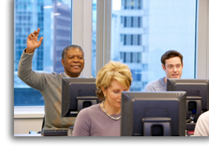 An adult class in a computer lab with a student raising their hand.