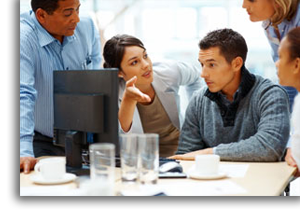 Employees standing around computer providing assistance and support.